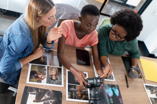 Preview: Diverse group of business colleagues brainstorming looking at photos in meeting room