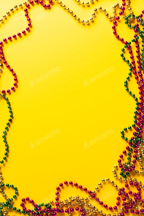 Preview: Composition of colourful mardi gras beads on yellow background with central copy space