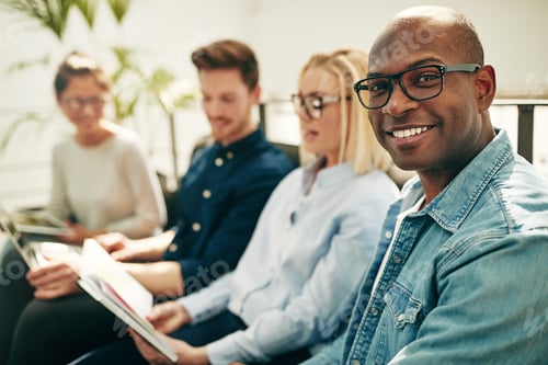 Preview: Smiling young African businessman sitting with coworkers in an office