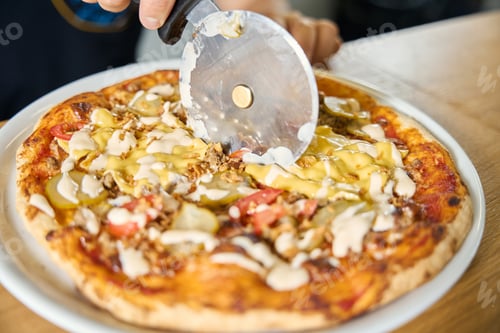 Preview: Skilled chef cutting fresh pizza into slices with special blade