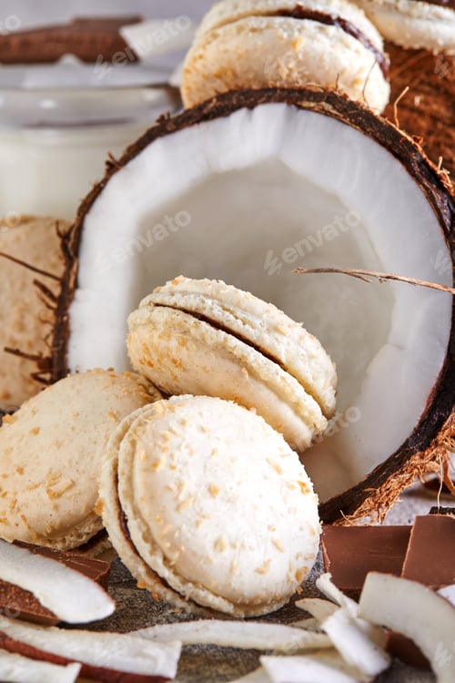 Preview: Coconut macarons with chocolate and coconut flakes on a table with a coconut in the background