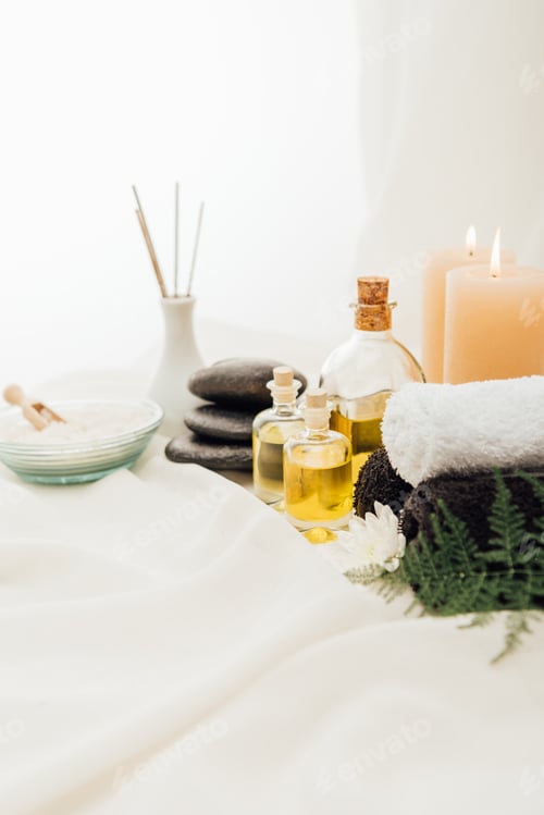 Preview: close up view of arrangement of spa treatment accessories with candles and pebbles on white