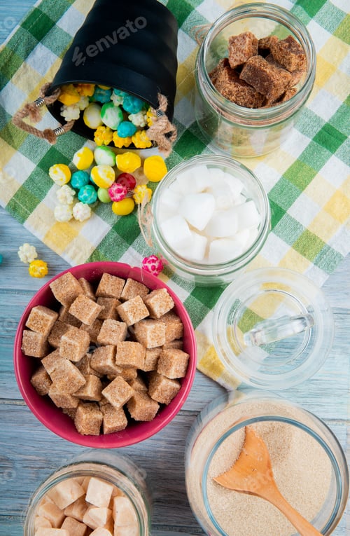 Preview: top view of various types of sugar in glass jars and colorful sugar candies scattered from a bucket