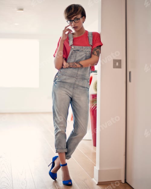 Preview: Young woman leaning on a wall in stylish overalls and blue heels