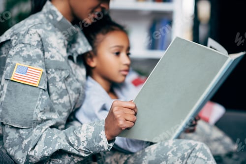 Preview: cropped view of african american daughter and mother in military uniform reading book together at