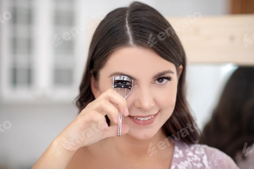 Preview: Young pretty full-figured smiling woman curling her eyelashes