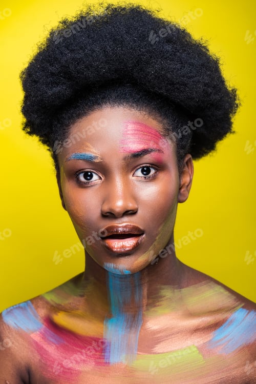 Preview: Surprised african american girl with bright makeup looking at camera isolated on yellow