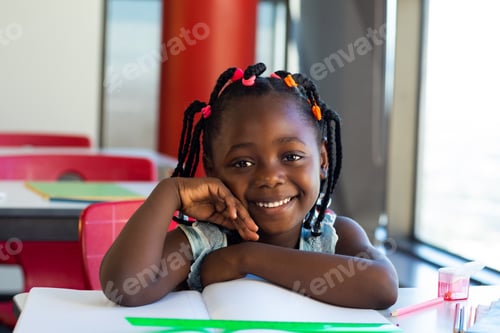 Preview: Portrait of happy african american schoolgirl sitting at desk and smiling at elementary school