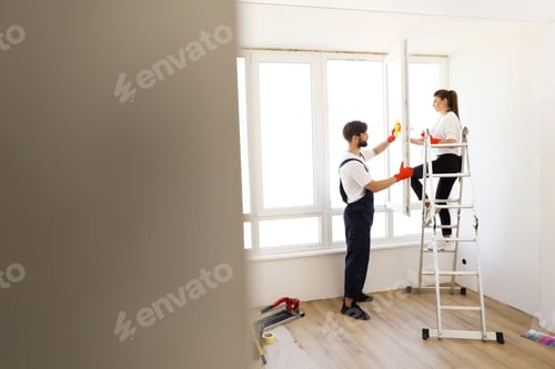 Preview: Beautiful caucasian couple wife and husband cleaning window together in room.