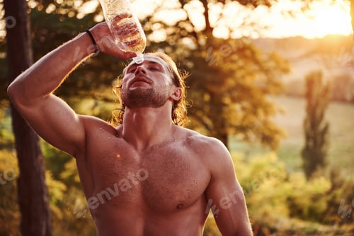 Preview: Refreshing with water. Handsome shirtless man with muscular body type is in the forest at daytime