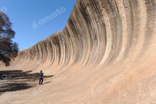 Preview: Woman standing at the foot of Wave Rock, a natural rock formation shaped like massive ocean wave