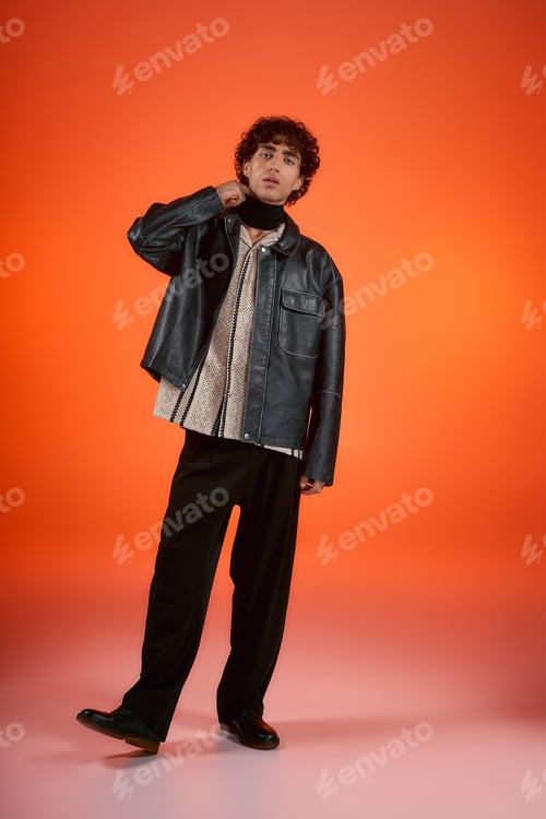 Preview: Stylish young man showcasing fashion against a vibrant orange backdrop in a creative setting