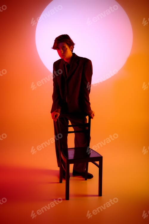 Preview: Stylish young man poses confidently with a chair against a bold sunset backdrop