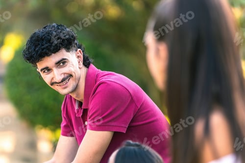 Preview: Man with modern hairstyle sitting on a bench while talking with other people