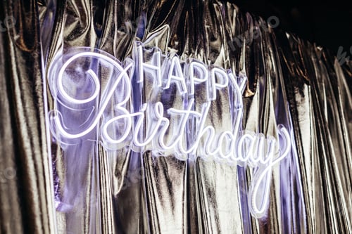 Preview: Happy birthday sign neon on silver curtain. Happy Birthday background. Party decor.