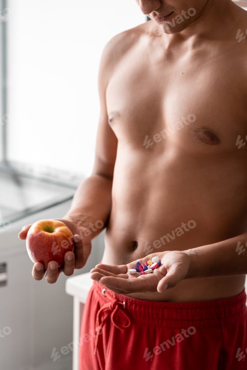 Preview: To eat or not to eat? Male holds pills and red apple. Choice between two sources of vitamins.