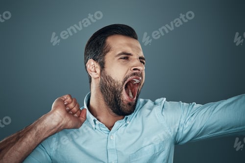 Preview: Yawning. Tired young man yawning while standing against grey background