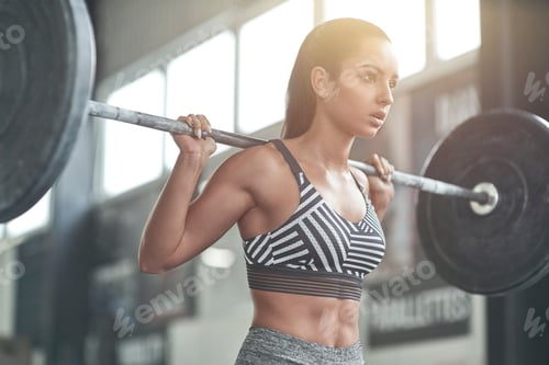 Preview: Young woman exercises in gym healthy lifestyle ready to lift bar