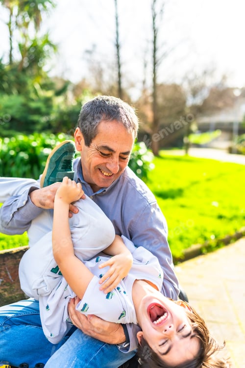 Preview: Grandfather tickling grandson in the park, authentic family moments