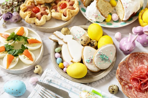 Preview: Easter table scene with an assortment of baking, desserts, stuffed eggs and dyed eggs.
