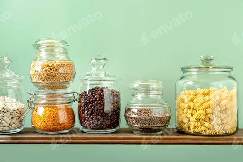 Preview: Different legumes in glass jars: chickpeas, pasta, beans, peas, lentils on green background.