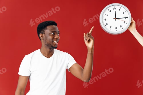 Preview: man of african appearance shows finger at watch red background