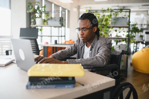 Preview: Focused african american student in wheelchair working on laptop in modern office