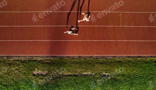 Preview: Aerial view of couple jogging on running track with long shadows