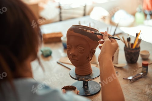 Preview: Young woman ceramist painting on clay sculpture in workshop