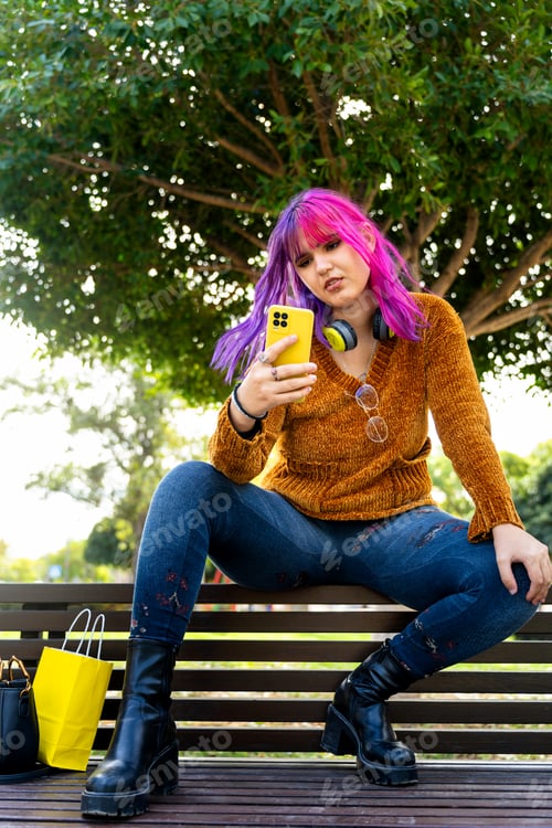 Preview: Body positive autistic girl with pink hair sitting on benches in a public park