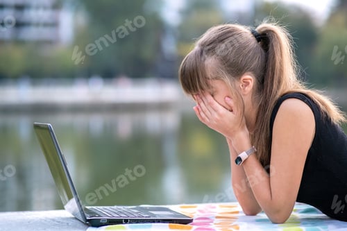 Preview: Exhausted young woman working behind laptop computer lying down in summer park outdoors. Problems