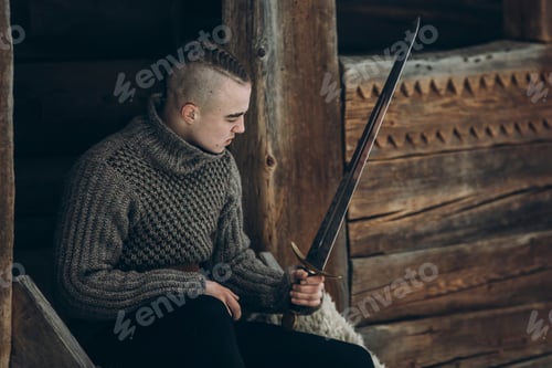 Preview: Portrait of strong viking warrior sharpening his sword, scandinavian viking cosplay