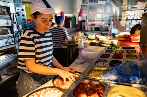 Preview: Pizza chef preparing pizza with various ingredients in london restaurant kitchen
