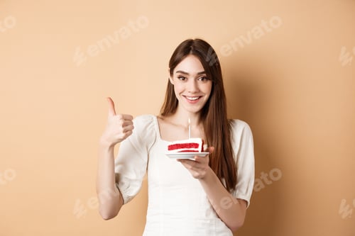 Preview: Beautiful birthday girl making wish on cake, showing thumb up and smiling happy, enjoying b-day