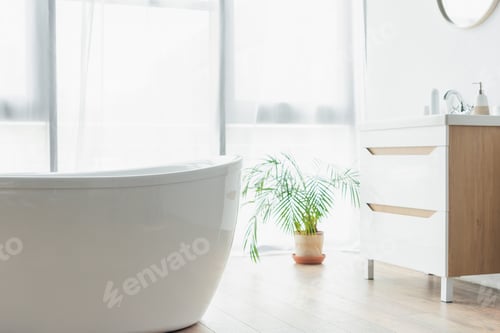 Preview: white bathtub near potted plant and sink with toiletries in modern bathroom