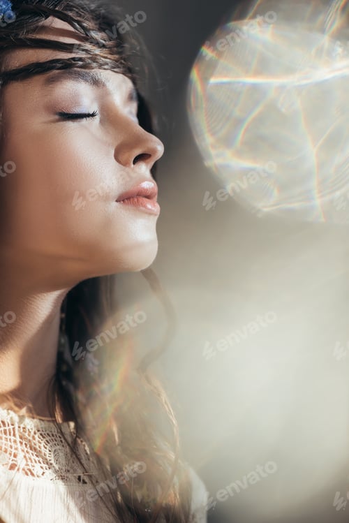 Preview: attractive boho girl with braids in hairstyle posing with closed eyes on grey with lens flares