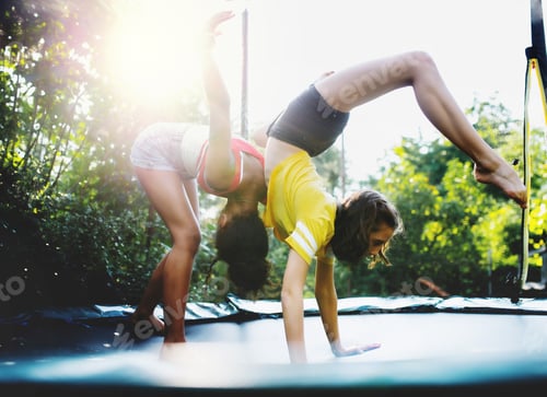 Preview: Front view of young teenager girls friends outdoors in garden, doing exercise on trampoline