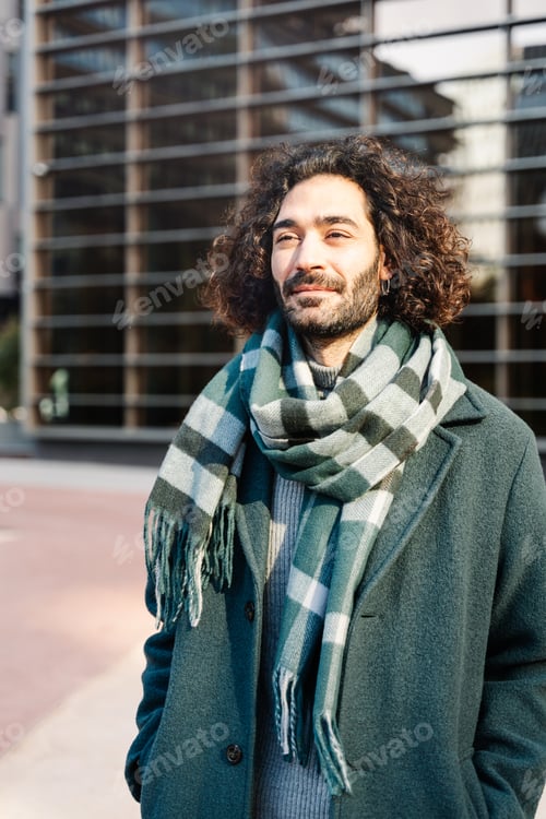 Preview: Young stylish professional man with long curly hair wearing a green scarf in the city in winter