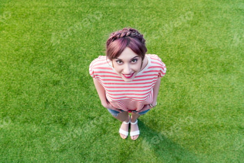Preview: high angle view of beautiful happy girl smiling at camera while standing on green grass