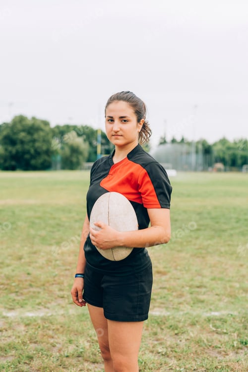 Preview: Confident young female rugby player holding a ball on the field.