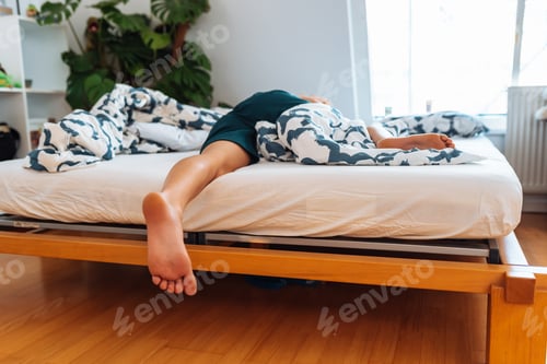Preview: young woman lies on bed with bare feet uncovered by blanket. feet close up