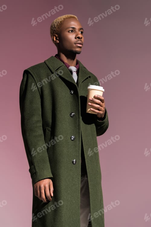 Preview: Stylish young african american man holding paper cup isolated on violet background
