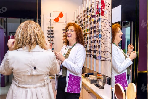 Preview: Smiling red-haired optician showing glasses to customers
