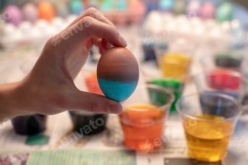 Preview: Boy holding up a dyed Easter Egg in front of cups of colored dye and other arts and crafts supplies