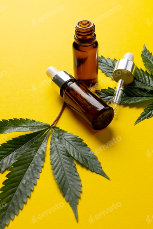 Preview: Vertical image of bottle of cbd oil and marihuana leaves on yellow surface