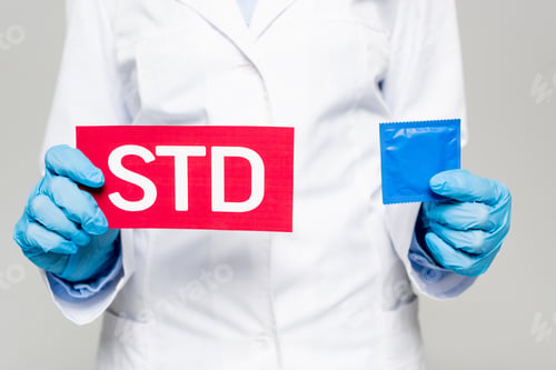 Preview: cropped view of doctor in white coat and latex gloves holding paper with std lettering and condom