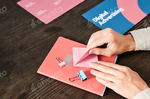 Preview: Hands of young office manager sitting by wooden table and taking pink notepaper