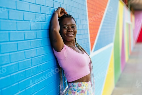 Preview: A African woman with long hair and a pink shirt is leaning against a wall