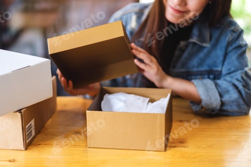 Preview: A beautiful young asian woman receiving and opening a postal parcel box at home for delivery