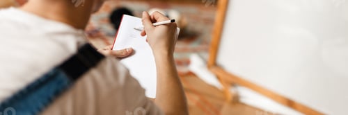 Preview: Young white man in headphones sketching while working on craft rug
